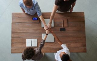 Four People Fist-Bumping Each Other While Sitting at a Desk