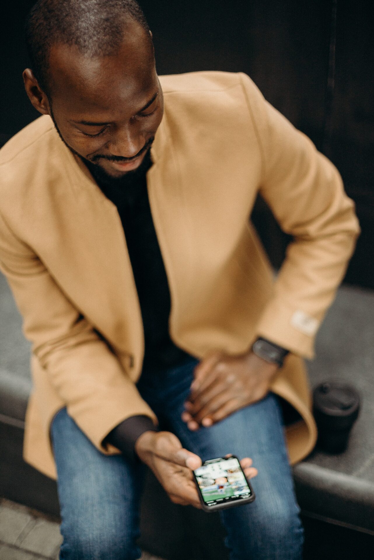 Man in camel-colored suit sitting down looking at his phone