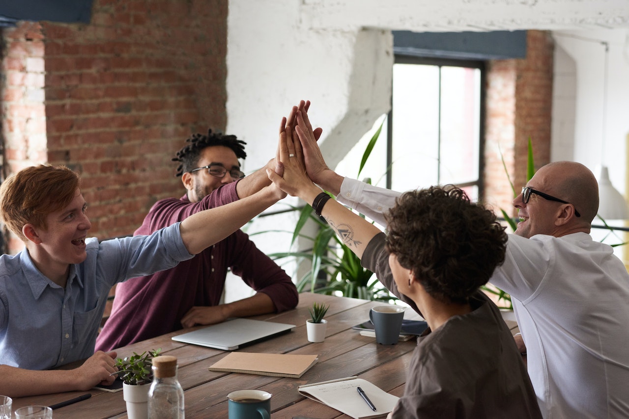 Team Members All High-Fiving Each Other While Sitting Around a Desk