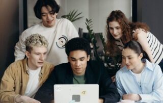 Photo of Group of People Looking at One Person Working on a Laptop