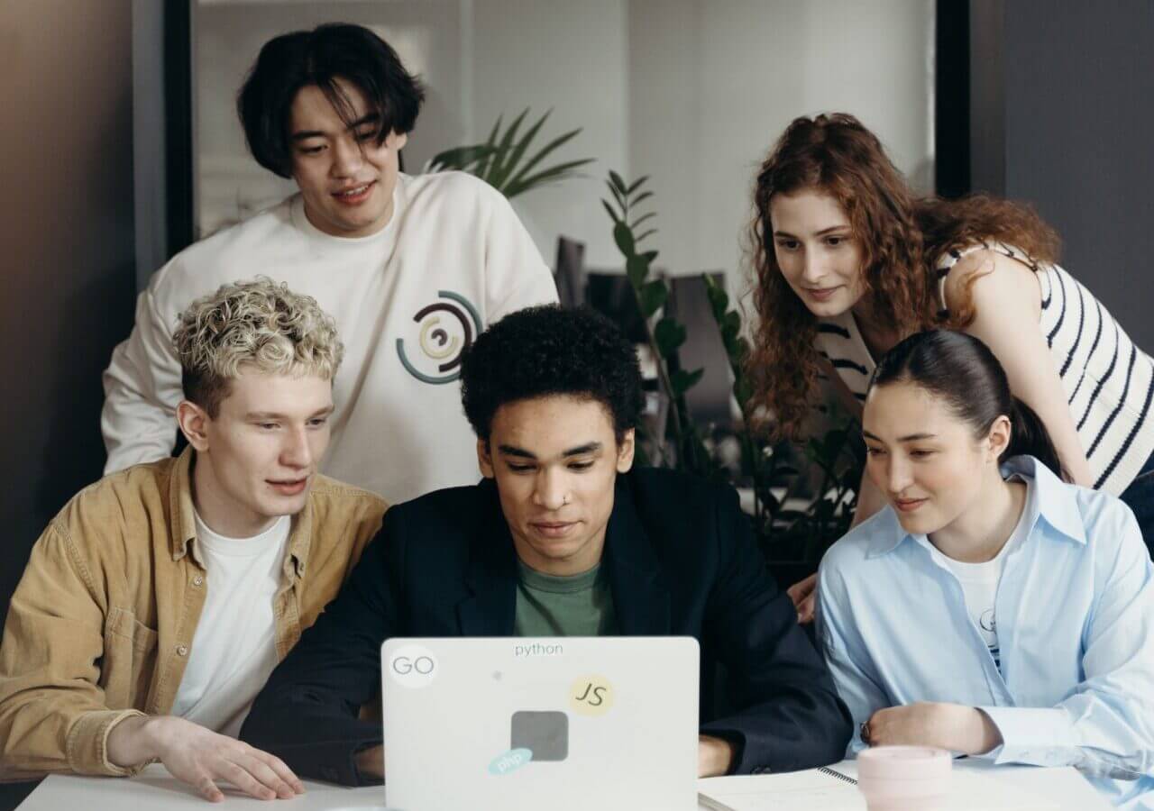 Group of People Looking at One Person Working on a Laptop