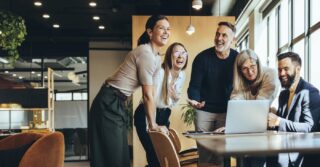 Coworkers Standing Around A Desk And Laughing