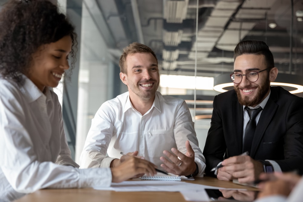 Smiling diverse colleagues having fun at briefing in office, employees enjoying fun conversation with business partner at meeting, discussing strategy, sharing startup ideas, team building activity