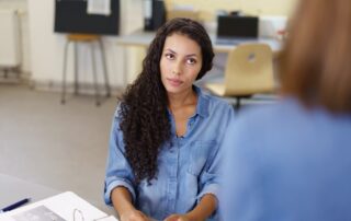 View over the shoulder of a co-worker of a pretty young businesswoman in a meeting passive-listening to a colleague in thoughts