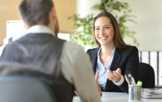 Two people having a discussion in an office setting, one person is gesturing with hands while the other listens attentively
