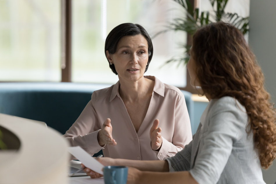 Two professionals engaged in a conversation, reviewing documents in a well-lit office setting.
